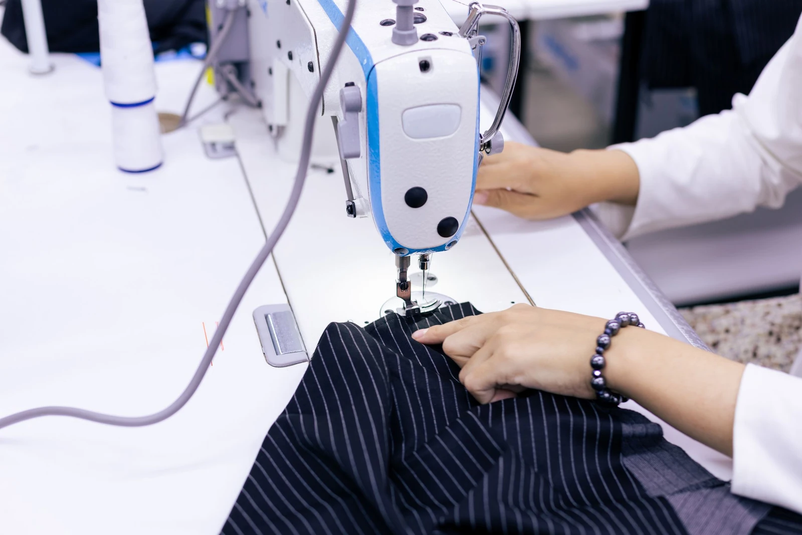 Mãos costurando tecido plano em máquina reta industrial de confecção