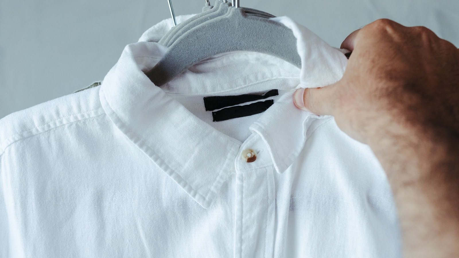 Close da gola, do pesponto e do botão de uma camisa branca de tecido plano