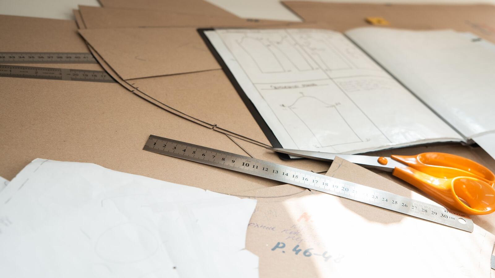 Moldes de papelão, desenho técnico, régua e tesoura sobre a mesa de uma confecção