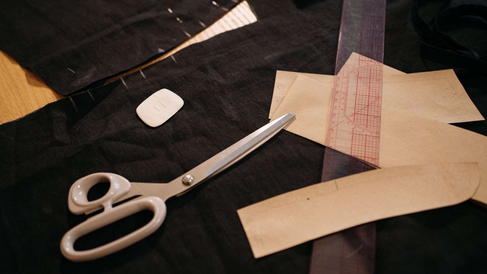 Moldes de papel, régua de modelagem, giz e tesoura sobre tecido na mesa de corte