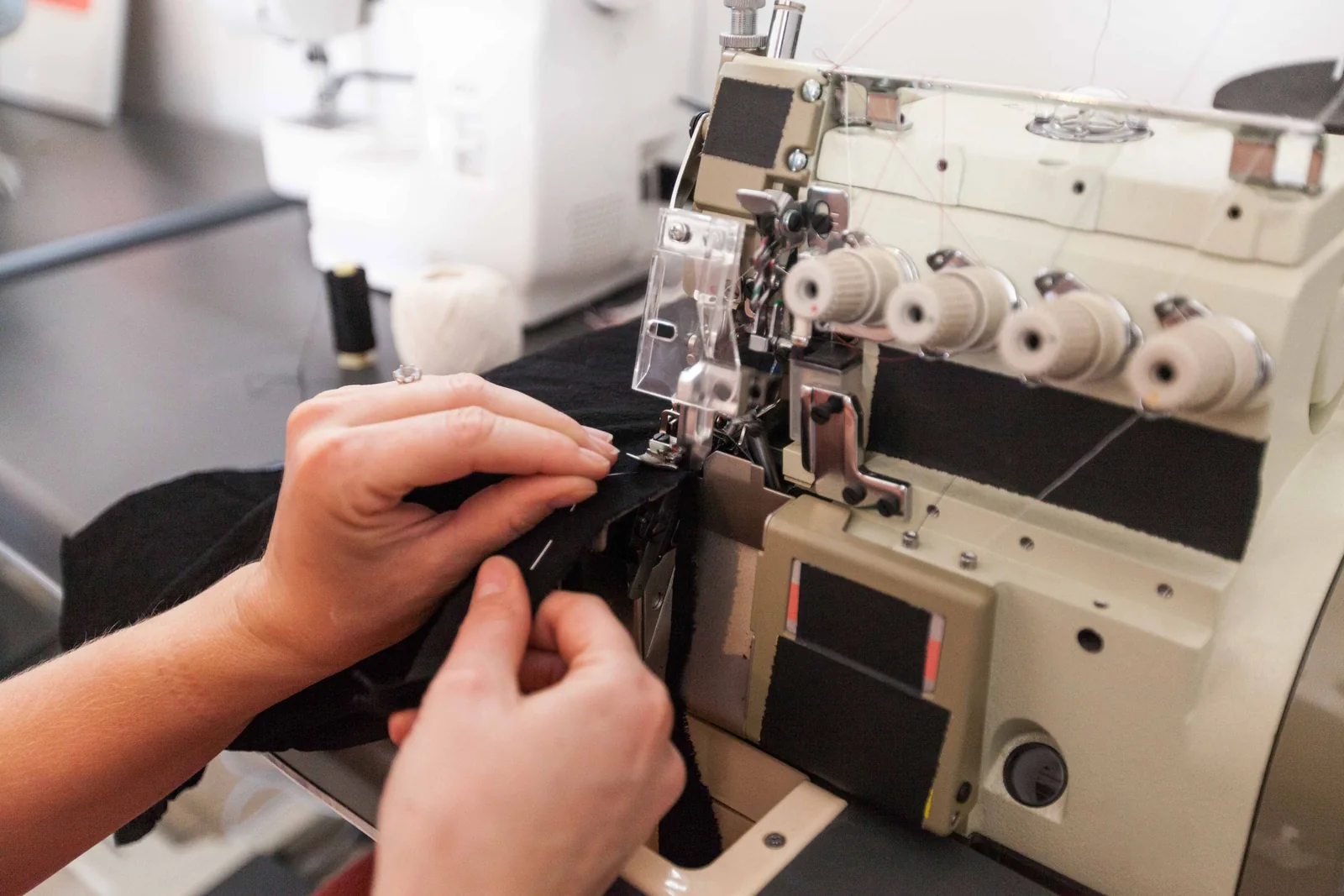 Mãos passando tecido em máquina overloque industrial de confecção