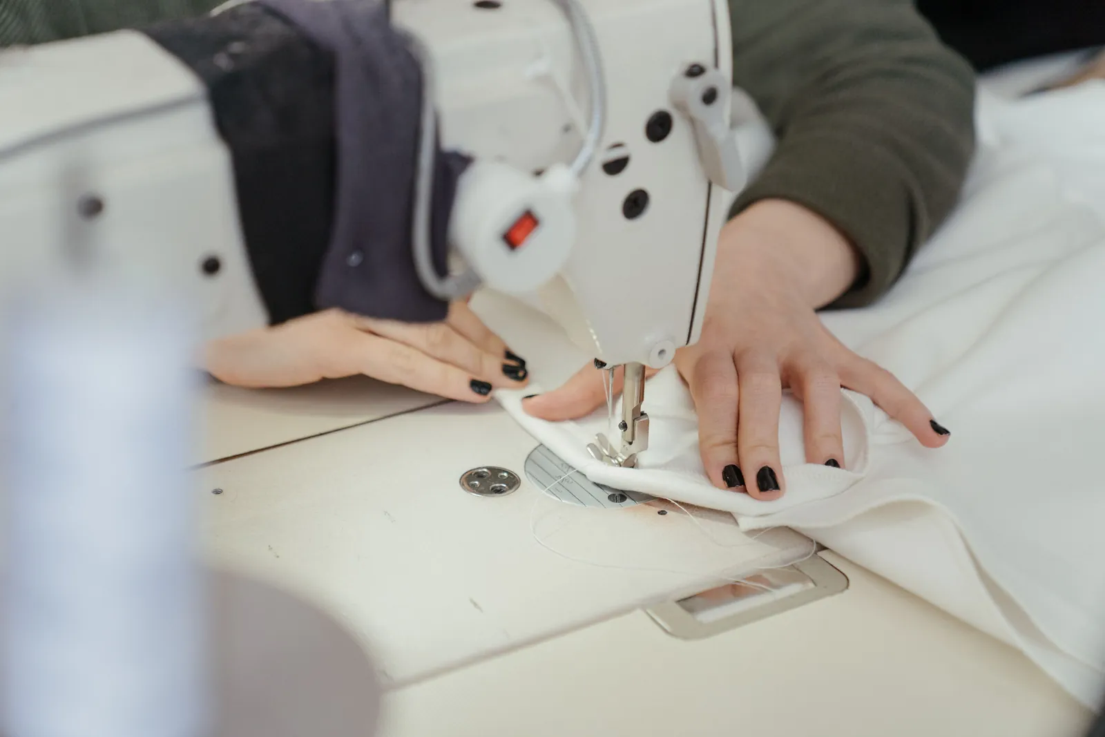 Mãos costurando tecido branco em máquina de costura industrial